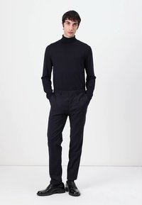 Navy turtleneck sweater with long sleeves, paired with dark trousers and black dress shoes. Smooth fabric and fitted design emphasize silhouette.