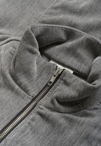 Grå zip-up jakke med høj krave, glat tekstur og kontrasterende sort lynlås med metalliske accenter.