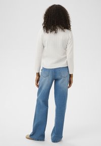 Pull en tricot blanc avec un motif texturé, associé à un jean large bleu clair. La tenue a une coupe décontractée et relaxante.