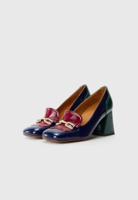 Scarpe con tacco caratterizzate da un corpo in pelle verniciata blu navy, un accento bordeaux con dettagli a catena e un tacco verde, con una superficie liscia.