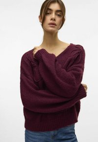 Bordeaux oversized trui met een diepe V-hals, textuur gebreid, en een losse pasvorm. Bevat kabelbrei details op de mouwen en een brede ribbenzoom.