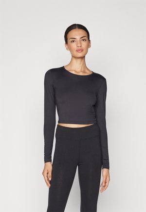 Top crop a maniche lunghe nero realizzato in materiale liscio e aderente, con scollatura rotonda e dettagli di cucitura, abbinato a leggings neri a vita alta.