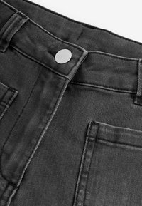 Schwarze Denim-Jeans mit einem Nahaufnahme-Blick auf den Bund, ausgestattet mit einem silbernen Metallknopf, kontrastierenden Nähten und aufgenähten Vorderentaschen.