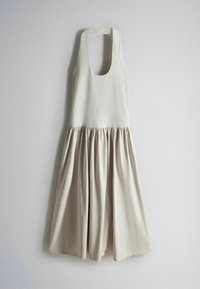 Robe sans manches crème avec encolure dégagée et jupe évasée plissée, suspendue sur un fond gris clair uni.