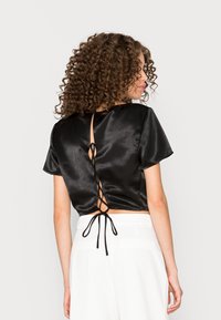 Top cropped de satin preto com mangas curtas, apresentando um design de costas lacadas e uma gola arredondada. Textura suave, estilo minimalista.