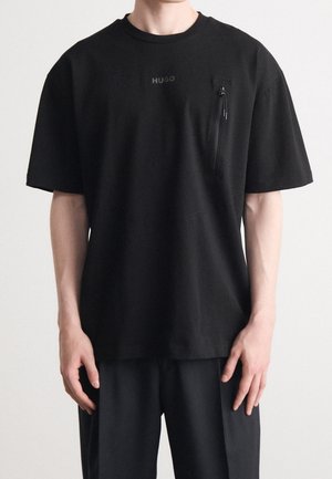 Czarna koszulka z krótkim rękawem wykonana z bawełny, z zamykaną na zamek kieszenią na lewej piersi i subtelnym logo marki. Gładka tekstura; luźny krój.