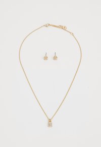 Gouden sieradenset met een delicate kettinghalsketting met een slotvormige hanger en studoorbellen, beiden versierd met kleine heldere stenen.