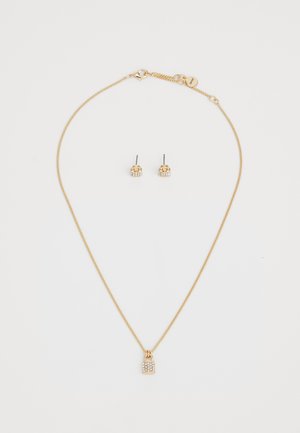Set di gioielli color oro composto da una delicata collana con catena e un ciondolo a forma di lucchetto, insieme a orecchini a bottone, entrambi decorati con piccole pietre trasparenti.