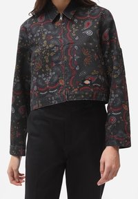 Kort denimjacka med en mörk bakgrund och färgglada paisleymönster i röd, gul och vit. Silverdragkedja fram.