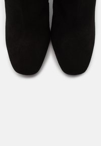 Paire de bottes en daim noir avec bouts carrés vues de dessus sur un fond blanc.