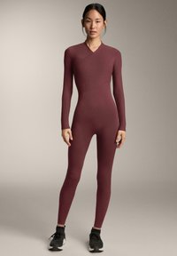 Mályva színű, hosszú ujjú body texturált, bordázott mintával, átfedő nyakkivágással és testhez simuló szabással, fekete tornacipővel párosítva.