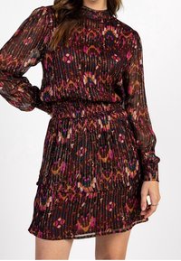 Vestido translúcido y multicolor con un estampado floral, cintura fruncida, mangas largas y un dobladillo con volantes. Los colores dominantes incluyen marrón, rosa y azul.