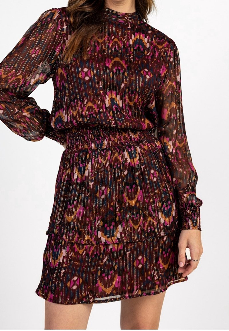 Vestido translúcido y multicolor con un estampado floral, cintura fruncida, mangas largas y un dobladillo con volantes. Los colores dominantes incluyen marrón, rosa y azul.