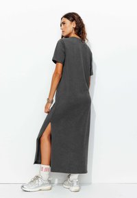 Robe maxi grise à manches courtes avec fente sur le côté, texture douce, coupe décontractée, assortie à des baskets argentées et des chaussettes à motifs.
