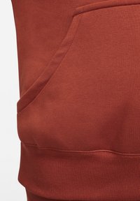 Tissu de sweat-shirt couleur rouille avec une poche kangourou, des poignets côtelés et une texture lisse, sans motifs ni accessoires visibles.
