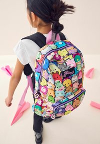 Bunt gemusterter Rucksack mit Comicfiguren, mehreren Farben, Reißverschlussfächern, schwarzen Trägern und einem pinken Griff. Glatte Stoffoberfläche.
