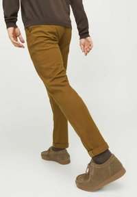 Pantalons en coton beige avec une coupe droite, ourlets retroussés et poches, associés à des chaussures en daim marron et des chaussettes marron.