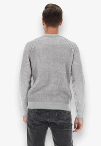 Maglione grigio a coste con maniche lunghe raglan, collo a giro e vita aderente. Mostrato dal retro con una texture liscia.