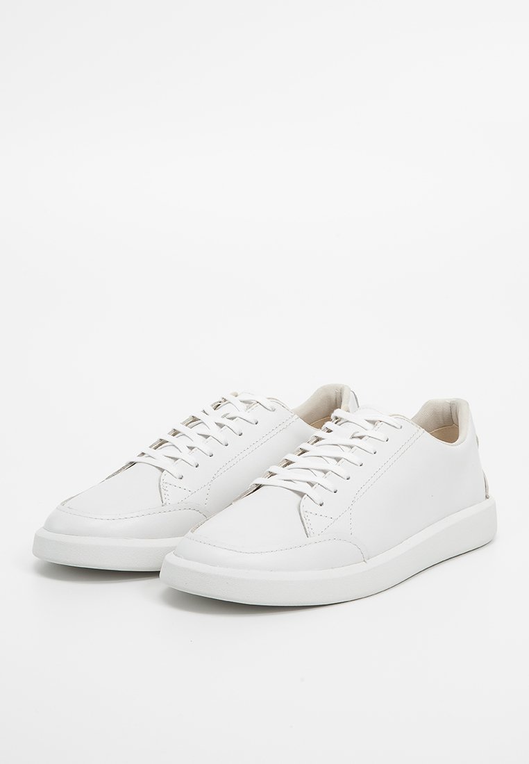 Baskets en cuir blanc avec une texture lisse, bout rond et semelle en caoutchouc plate. Présente des lacets et des accents de design minimalistes.