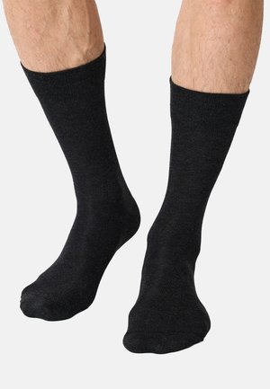 Legs wearing plain black mid-calf socks on a light gray background, showing fit and texture of the fabric.