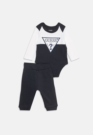 Body bébé manches longues noir et blanc avec logo GUESS et pantalon noir assorti sur fond uni.