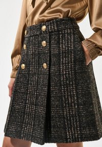Falda a cuadros negra y marrón con forma acampanada, que presenta detalles en botones dorados y bolsillos laterales. Fabricada en tejido texturizado.