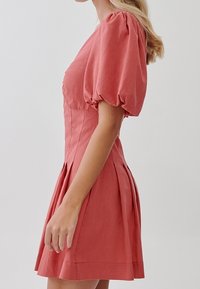 Krátké šaty s puff rukávy v korálově růžové barvě. Přiléhavý korzet s skládací sukní. Vyrobeno z lehkého materiálu s hladkou texturou.