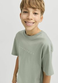 Zaļš kokvilnas T-krekls ar īsām piedurknēm, ar baltu "JACK & JONES" logo uz priekšpuses, apaļā kakla dizains un mīksta tekstūra.