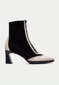 Svarta mocka ankelstövlar med dragkedja, som har en ljusbeige lädertå och klack, samt en texturerad svart rem längst fram.