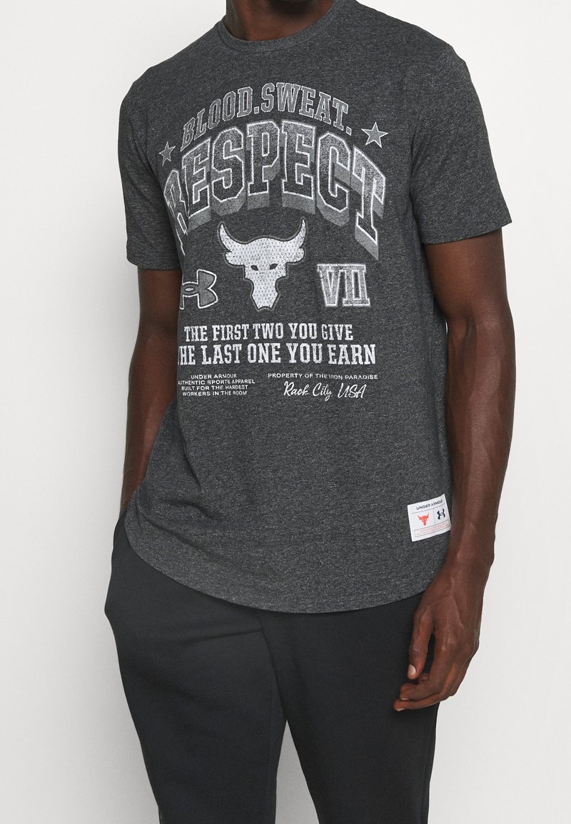 Homme portant un t-shirt gris foncé avec le texte "Blood. Sweat. Respect" et un logo de taureau, assorti à un pantalon noir.