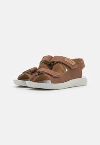 Sandalias de cuero marrón con lados recortados, dos correas de Velcro y una suela de goma blanca. Presenta una etiqueta del logo de Geox en el lateral.