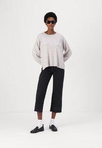Világosszürke, oversized pulóver bordázott aljjal, fekete cropped farmernadrág bolyhos szélekkel, fekete loaferek és fehér zoknik; a modellen napszemüveg van.