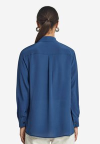 Blaues Langarmhemd mit glatter Textur, Rückenpasse und geradem Saum. Verfügt über knöpfbare Manschetten und einen Kragen.