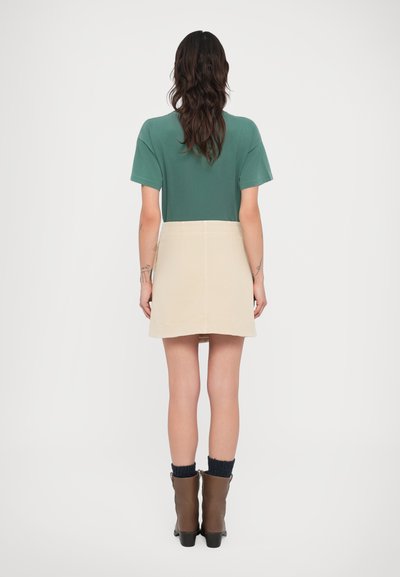 Πράσινο τοπ με κοντά μανίκια συνδυασμένο με μπεζ φούστα. Η φούστα έχει ομαλή υφή και ίσια κοπή. Καφέ μποτάκια αστραγάλου με μπλε-ναυτικό κάλτσες.