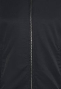 Giacca nera con zip centrale, texture liscia e due tasche laterali. Il tessuto appare resistente con una finitura opaca.