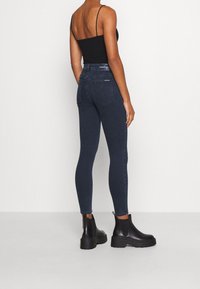 Mörkblå slim fit-jeans med hög midja, med subtila sömnadsdetaljer och en jämn textur, kombinerat med svarta ankelskor.