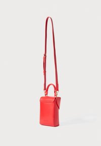 Small rectangular red leather crossbody bag with top handle and adjustable long strap against white background.