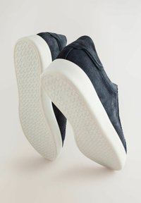 Zapatillas de ante azul oscuro con suelas de goma blanca, mostradas en un ángulo para mostrar ambos lados y las suelas texturizadas.