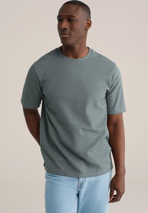 Grijs T-shirt met korte mouwen gemaakt van een gestructureerde stof. Rondhalsontwerp met een comfortabele pasvorm, gecombineerd met lichtblauwe spijkerbroek.