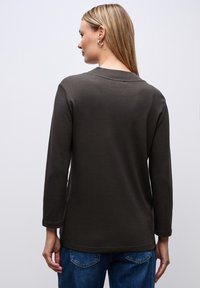 Lange mouwen, donkergrijze shirt van zachte stof, met een ronde halslijn en een losse pasvorm, gecombineerd met blauwe spijkerbroeken.