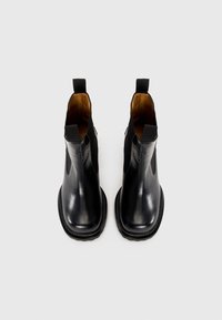Une paire de bottes Chelsea en cuir noir avec des languettes de tirage et des semelles épaisses, présentée de dessus sur un fond clair.