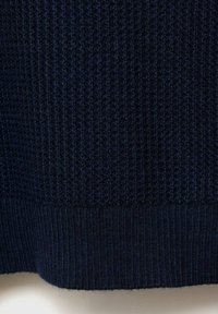 Mörkblå stickad tyg med en texturerad ribbad mönstring och en slät, bred mudd i botten. Det övergripande utseendet är tätt och intrikat.