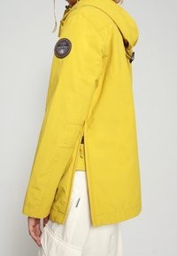 Gele waterdichte jas met capuchon, voorzien van zijritsen en een ronde patch op de bovenmouw. Gladde textuur, casual pasvorm.