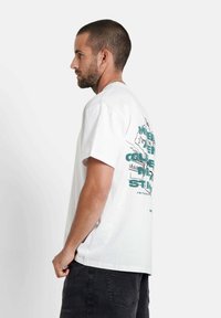 Witte katoen t-shirt met korte mouwen, met een grafisch ontwerp in het groen op de achterkant. Losse pasvorm, rechte zoom en casual stijl.