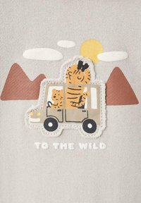 Beige tyg med en broderad design av ett brunt fordon med två tigrar, berg och moln. Texten lyder "TILL VILDERN".