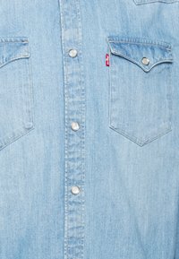 Vaaleansininen farkkupaita, jossa on kaksi rintataskua, hopeanväriset napit ja teksturoitu kangas. Vasemmassa taskussa on Levi's-logo.