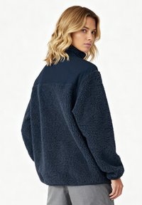 Pull-over en polaire marine avec col montant, extérieur texturé, et panneau d'épaule lisse contrastant ; coupe ample et poignets côtelés.