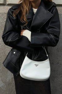 Veste en cuir noir avec revers, grand col et détails de poches. Sac à main en cuir blanc avec un logo triangulaire et une forme arrondie.