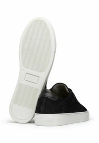 Svarta mockaskor med en slät svart skinnklack och vit gummisula, med en strukturerad botten för grepp och en minimalistisk design.