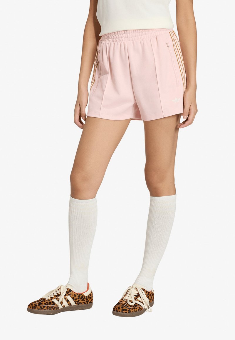 Personne portant un short de sport rose clair avec des rayures orange et des chaussettes blanches montantes, associée à des baskets à imprimé léopard.